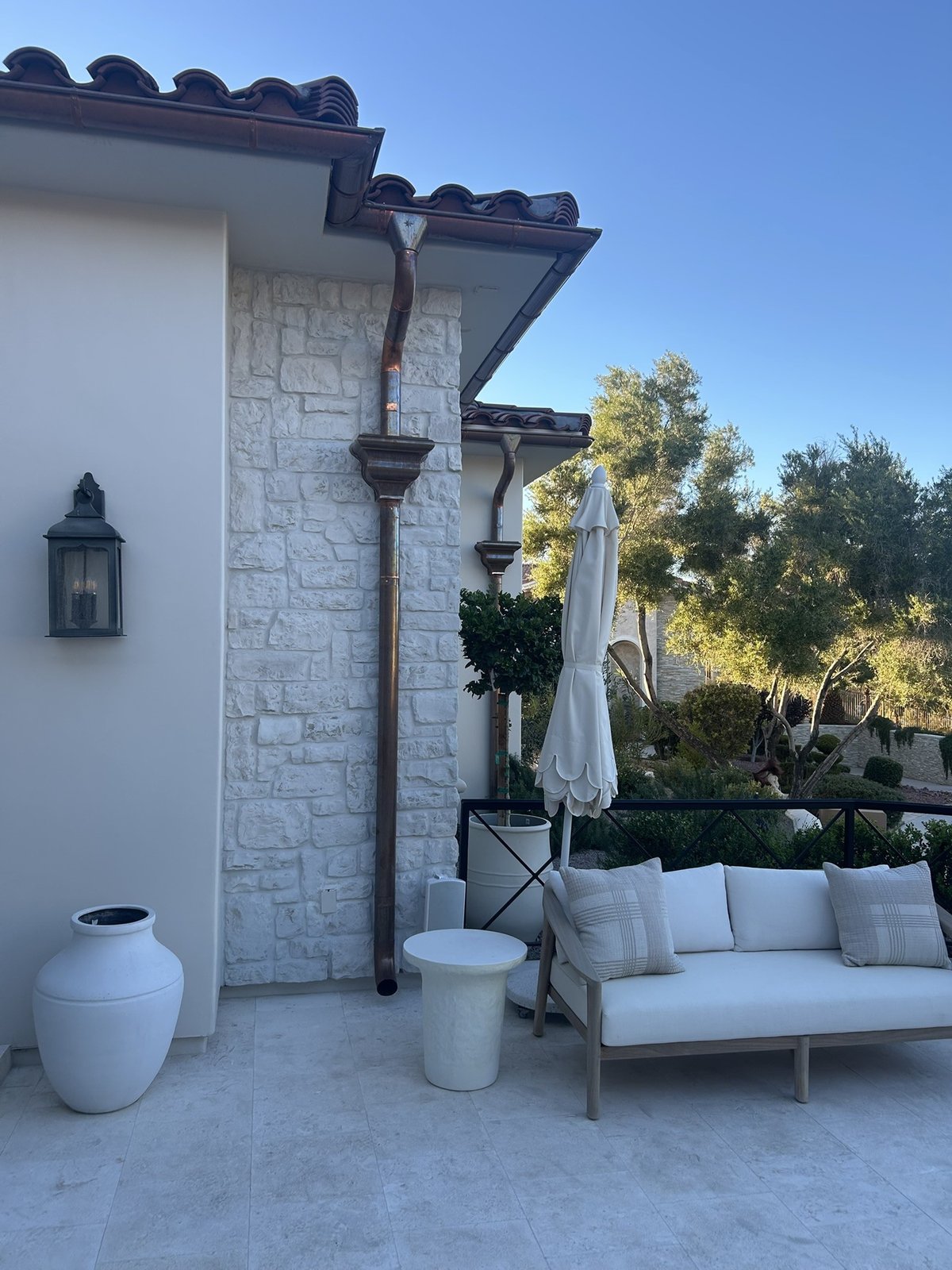 Copper gutter, copper leader head and round copper downspout darkened to a deep brown on a stone wall of the same Anthem home
